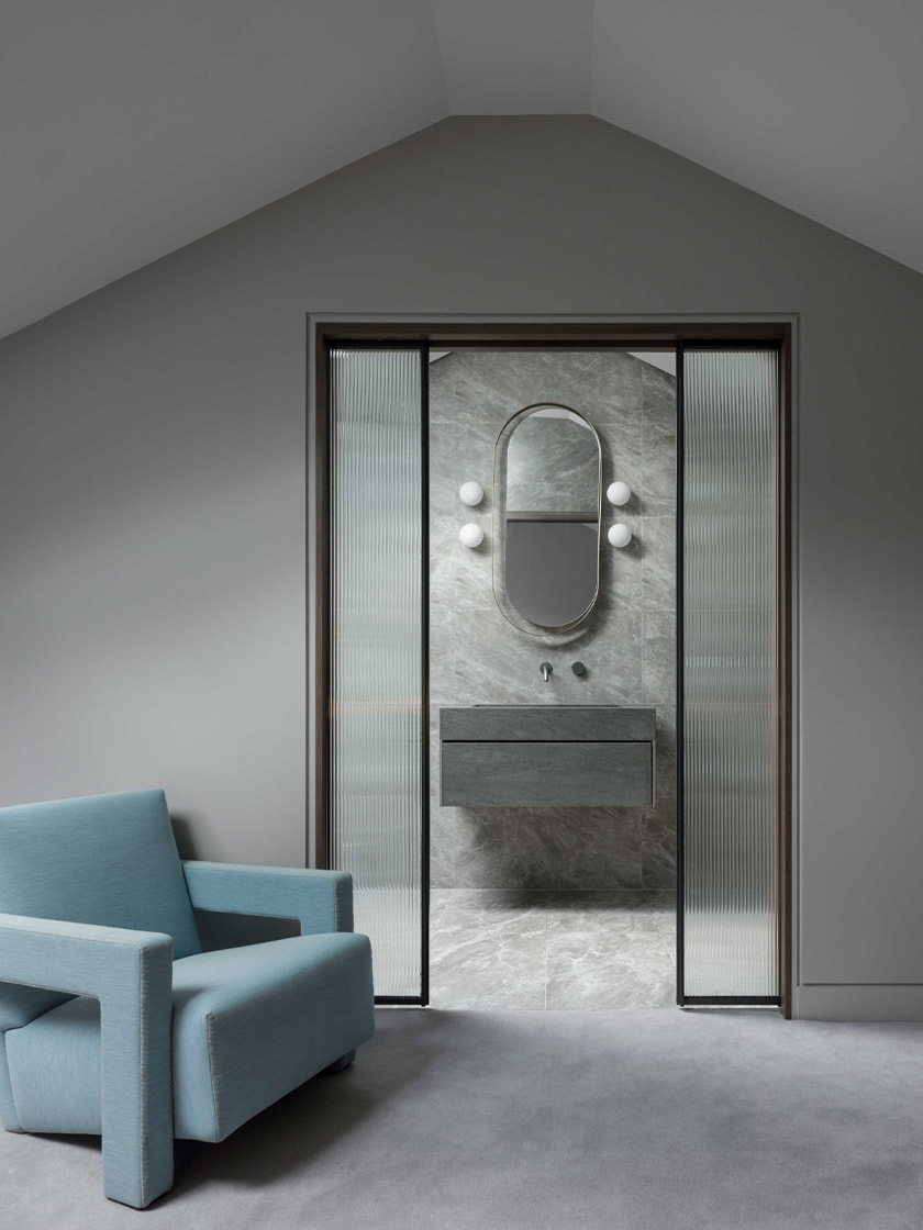 A bathroom entrance framed by frosted glass sliding doors, leading into a space with a gray marble wall, a floating vanity, and an oval mirror with soft lighting.