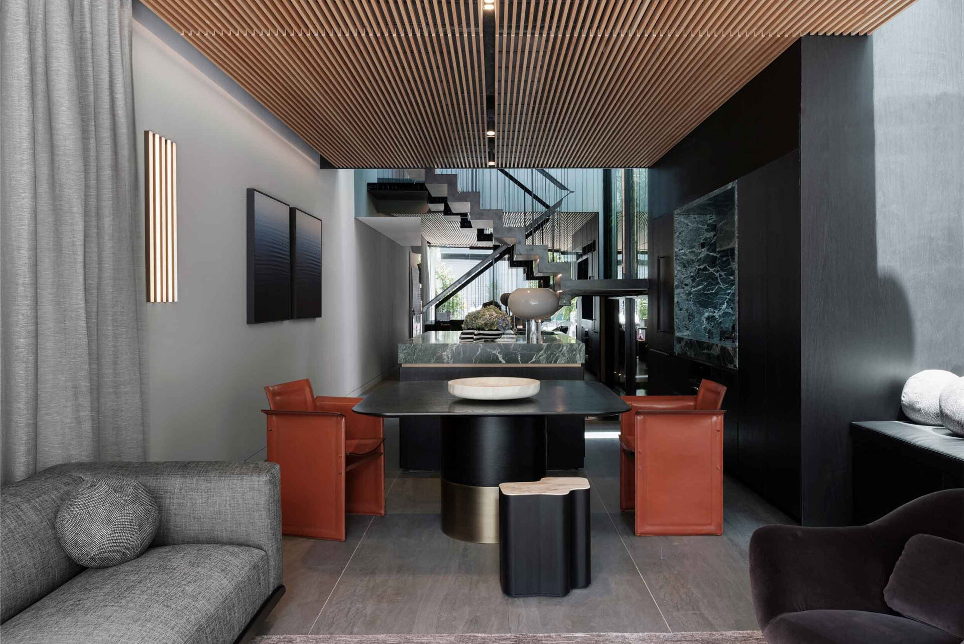 A view of the open-plan living and dining area in The Glasshouse by Nina Maya Interiors, with a black dining table, leather chairs, and modern decor, under a wooden slatted ceiling.