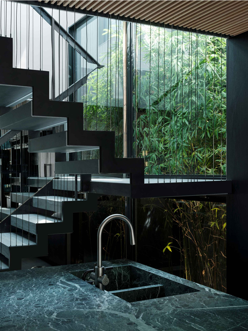 Modern Staircase with Green Marble: A striking staircase with black metal steps and thin, vertical wire railings, surrounded by glass walls. The staircase is adjacent to a kitchen area with a green marble countertop and sink, with lush bamboo visible through the glass.