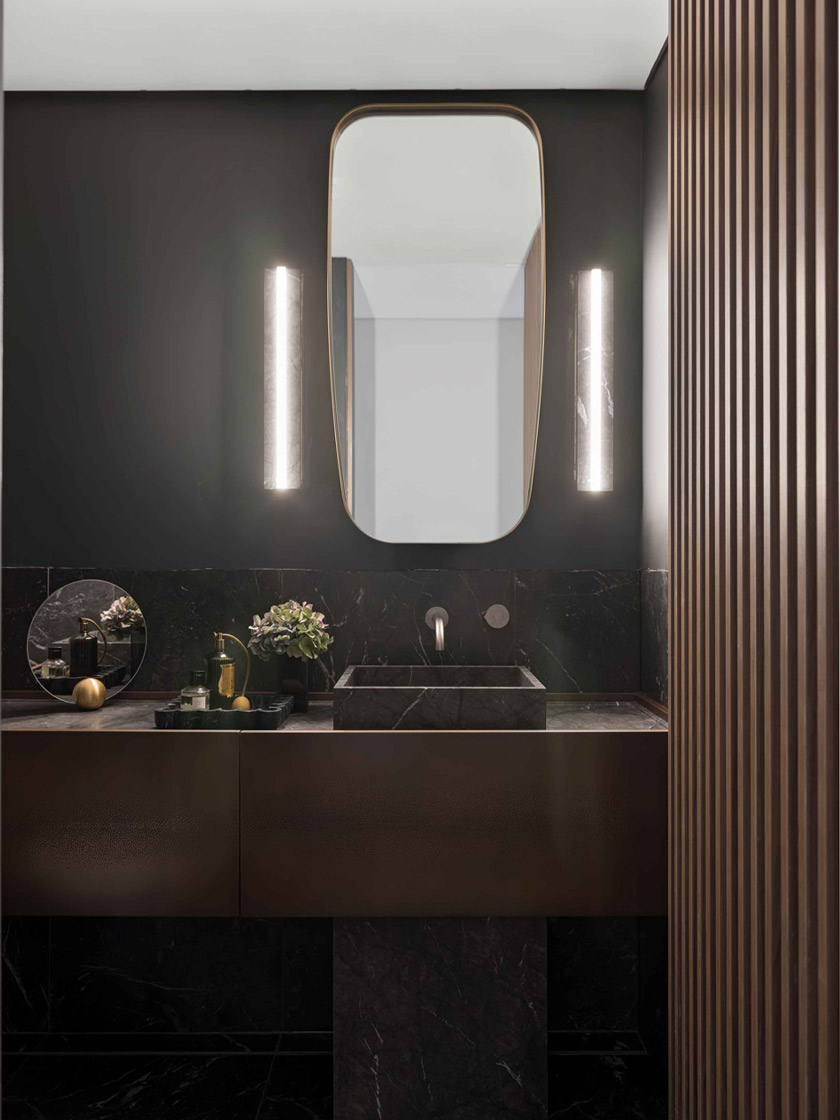 A modern bathroom in The Glasshouse by Nina Maya Interiors, with a black marble vanity, sleek lighting, and a minimalist mirror, creating a refined and elegant space.