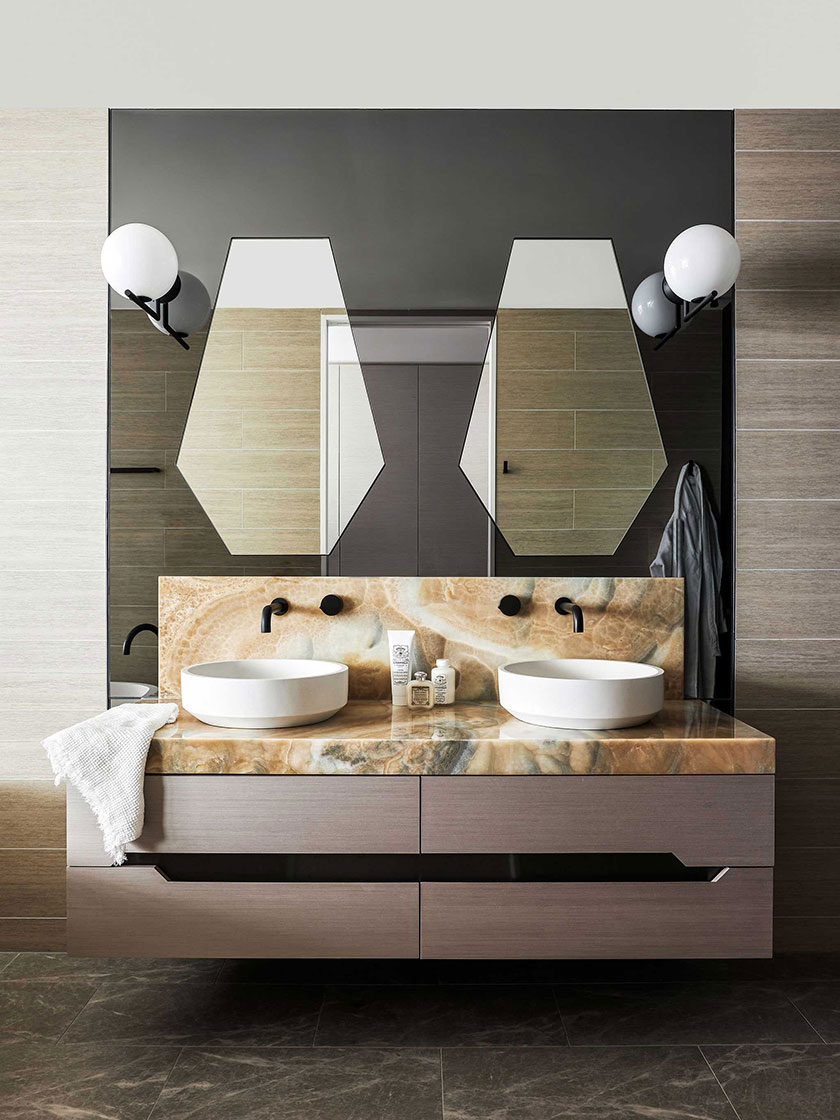 A modern bathroom in the Jewel Apartment by Nina Maya Interiors, featuring a double vanity with marble countertops, geometric mirrors, and stylish lighting fixtures.