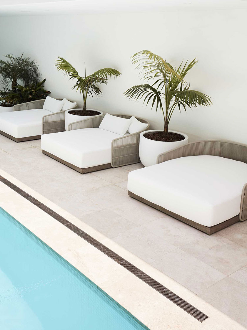 Poolside lounge area with white cushions and potted plants, designed by Nina Maya Interiors.