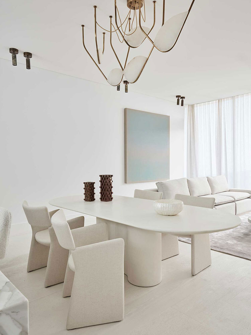 Minimalist dining room designed by Nina Maya Interiors, featuring a white oval table, beige upholstered chairs, modern chandelier, and neutral-toned decor.