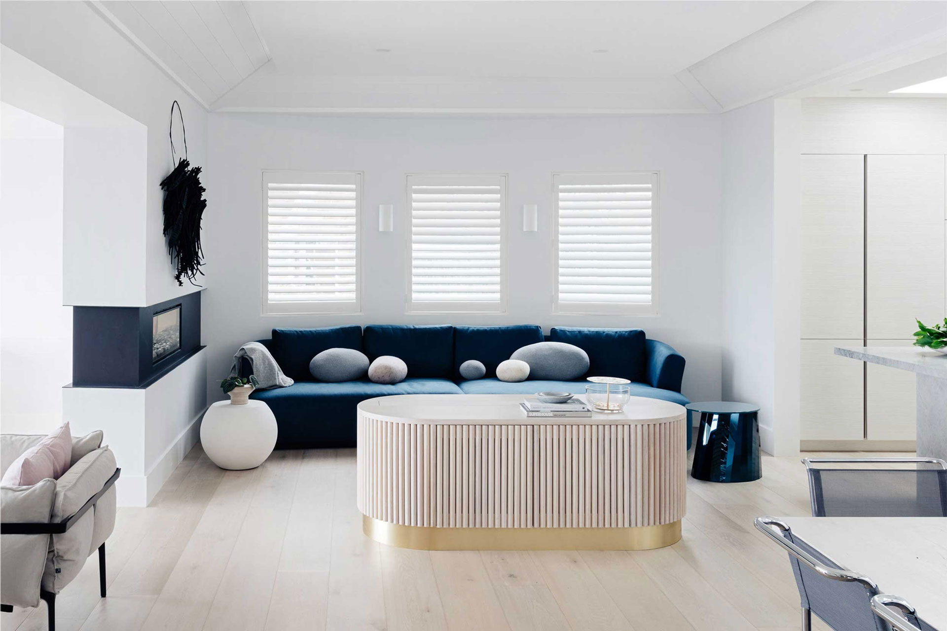 Ocean Pearl Villa - Palm Beach: A cozy lounge area featuring a deep blue velvet sectional sofa, white oval coffee table, and a modern fireplace, designed by Nina Maya Interiors.