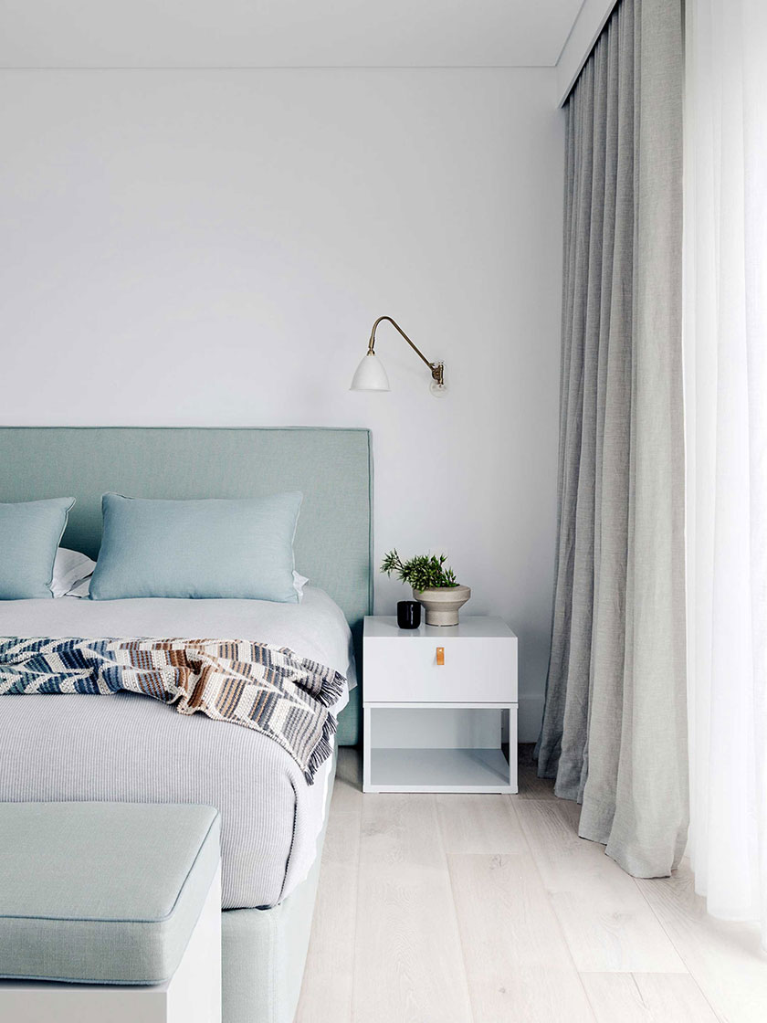 Ocean Pearl Villa - Palm Beach: Bedroom with a soft, muted color palette, including a pale green upholstered bed, white nightstand, and sheer curtains, designed by Nina Maya Interiors.