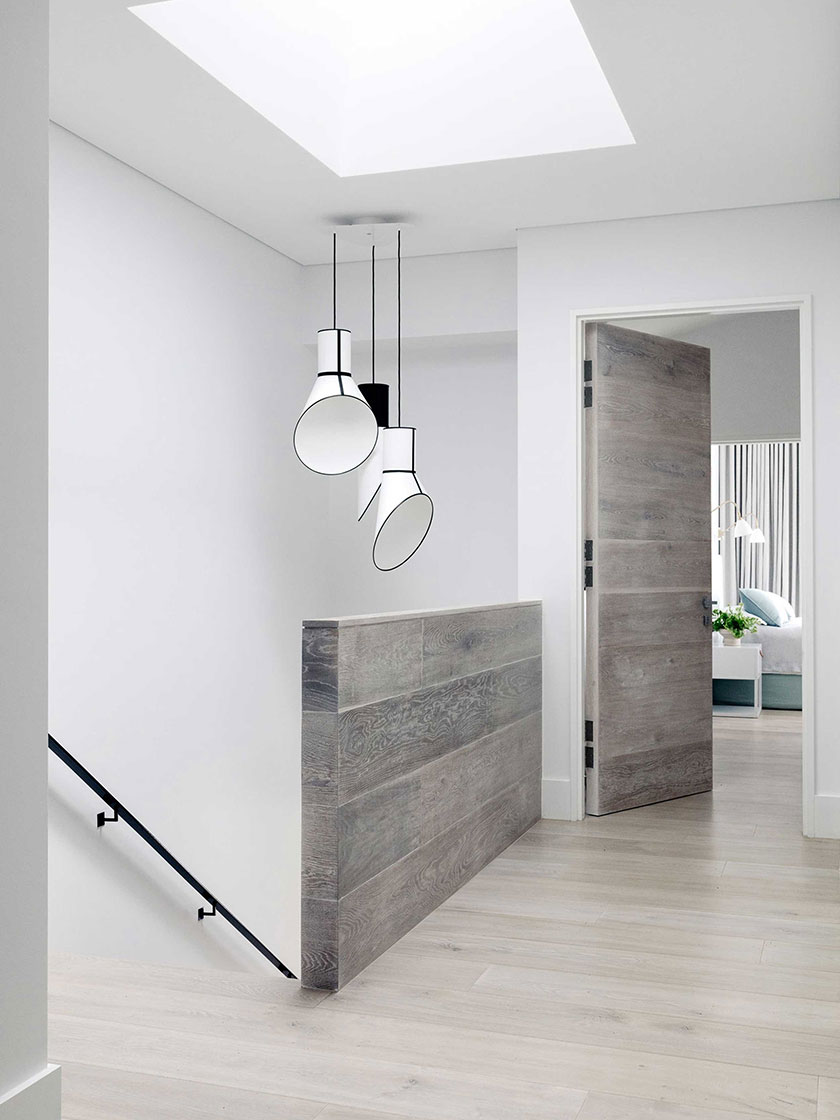 Ocean Pearl Villa - Palm Beach: A hallway with natural light pouring in through a skylight, featuring a minimalist staircase and modern lighting fixtures, designed by Nina Maya Interiors.