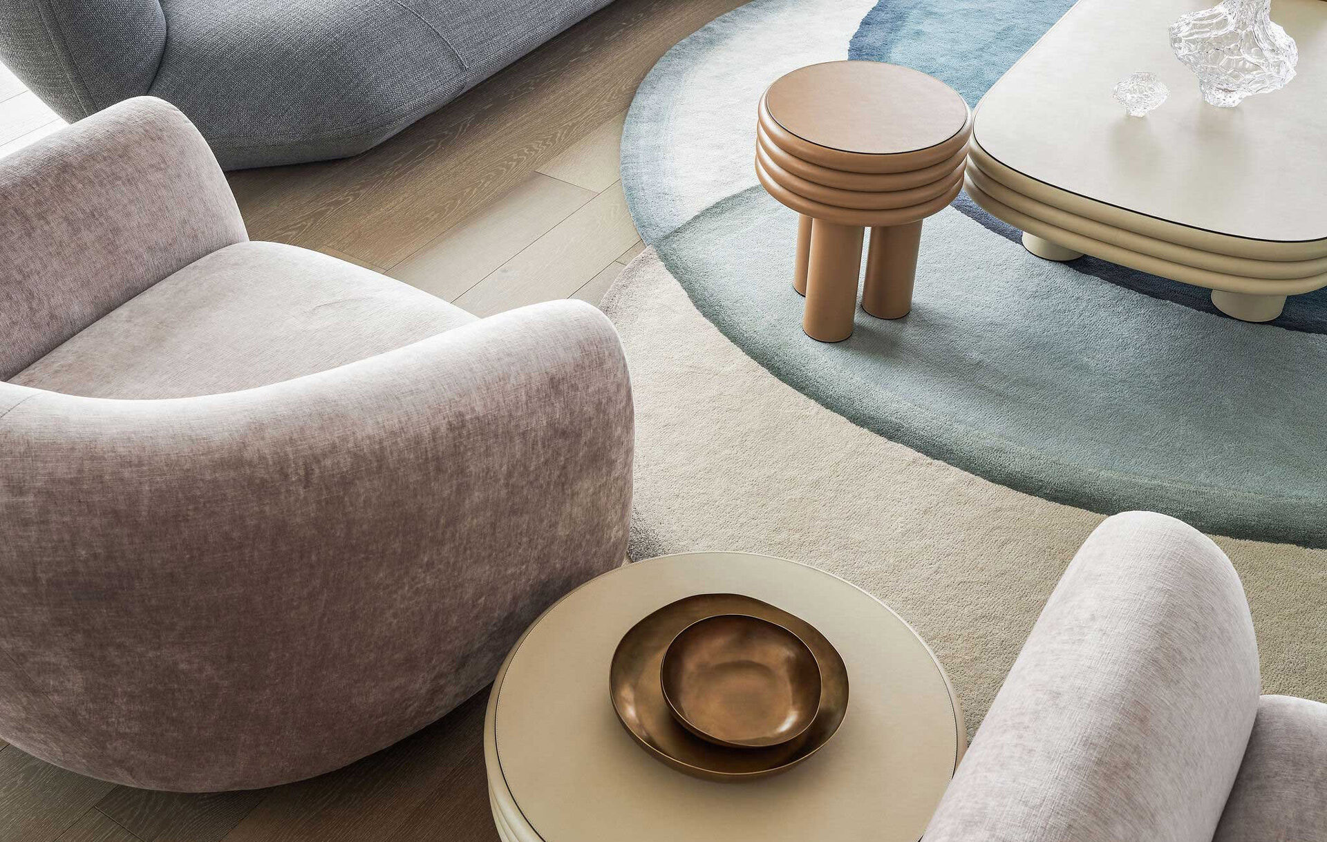 An overhead view of a cozy seating area in the Jewel Apartment, designed by Nina Maya Interiors, with a light pink armchair, round beige coffee table, and a circular rug with shades of blue and beige.