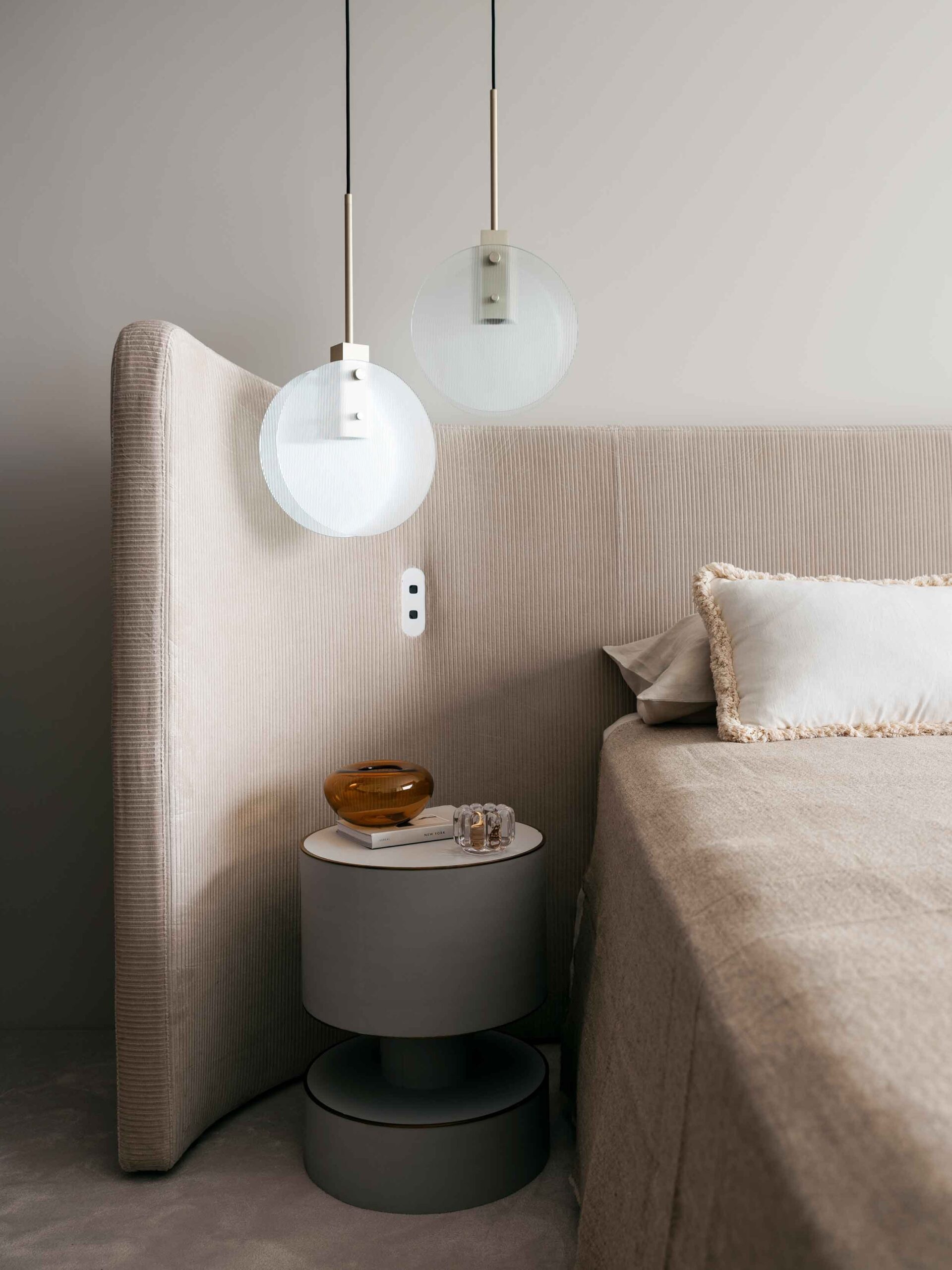 A cozy bedroom designed by Nina Maya Interiors featuring a beige upholstered bed with matching bedside tables, pendant lights with glass globes, and a neutral palette that exudes calm and sophistication.