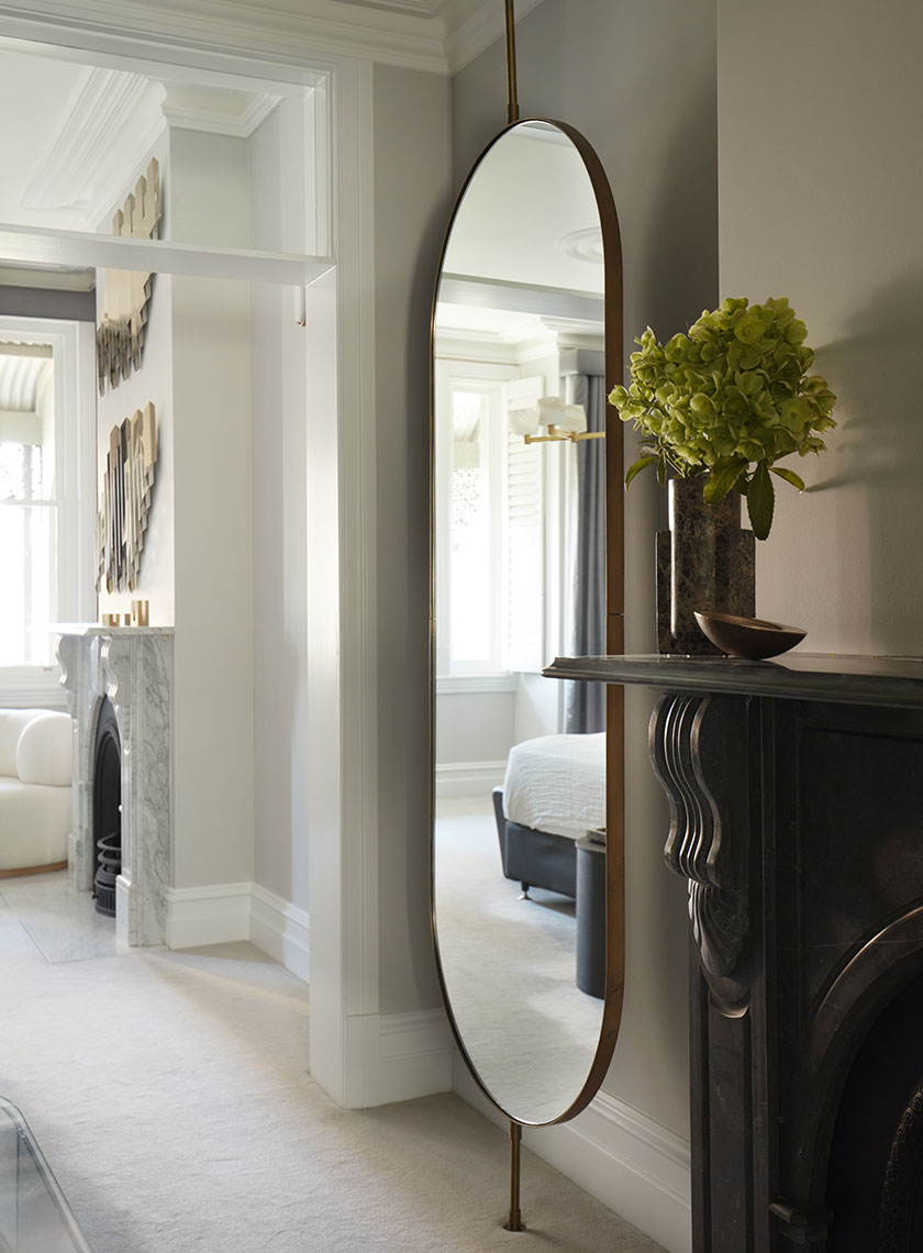 Large Arched Mirror by Fireplace: A tall, arched mirror set above a black mantelpiece, with a vase of green flowers and a glimpse into a luxurious bedroom. Interior design by Nina Maya Interiors at Residence K, Potts Point.