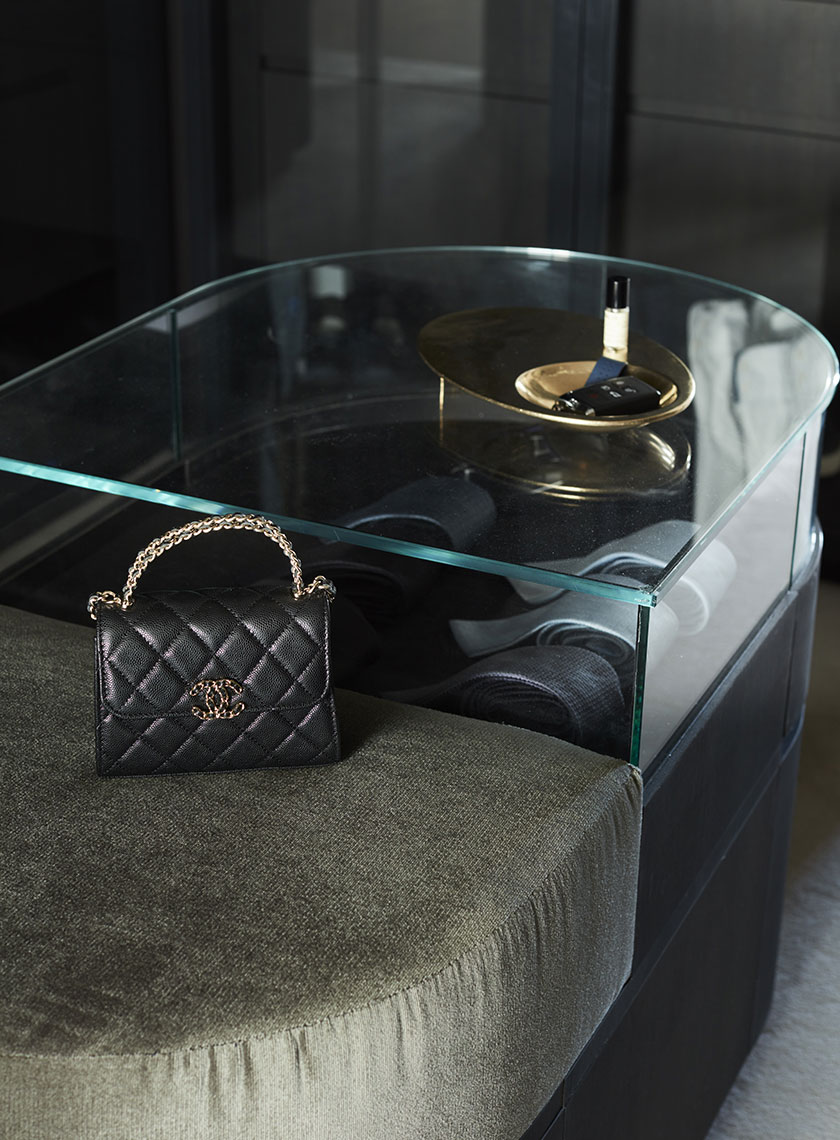 Chanel Bag on Glass-Topped Ottoman: A close-up of a black Chanel handbag resting on a glass-topped ottoman, part of a sophisticated closet space. Designed by Nina Maya Interiors at Residence K, Potts Point.