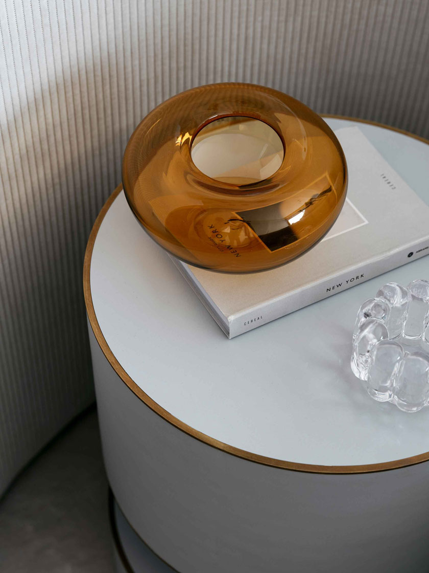 A close-up of a stylish bedside table featuring a round amber glass vase and a book titled "New York," part of Nina Maya Interiors' design for Residence R.