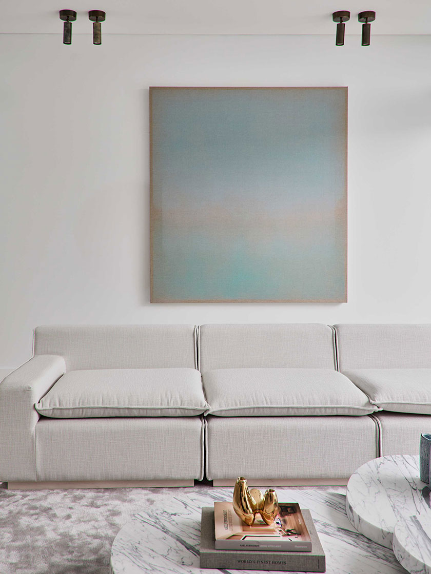 Contemporary living room by Nina Maya Interiors, with a white sofa, large abstract artwork, and marble coffee table with decorative books and gold accents.