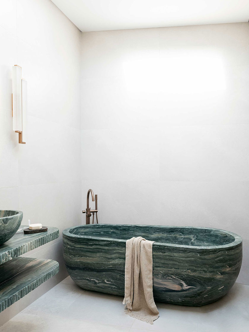 Luxurious bathroom featuring a green marble bathtub, matching sink, and modern fixtures, designed by Nina Maya Interiors.