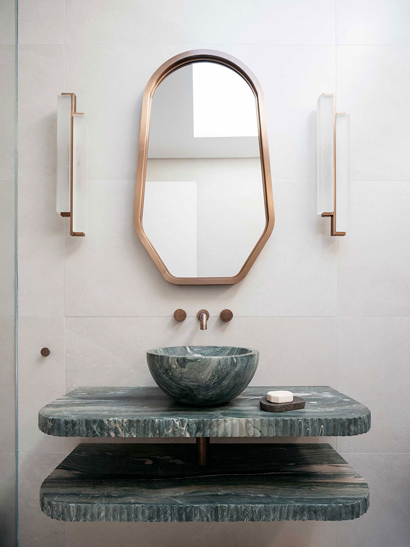 Modern bathroom vanity with a green marble sink, unique mirror, and contemporary lighting, designed by Nina Maya Interiors