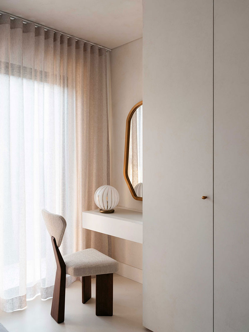 Cozy corner with a small vanity, white chair, and sheer curtains, designed by Nina Maya Interiors.