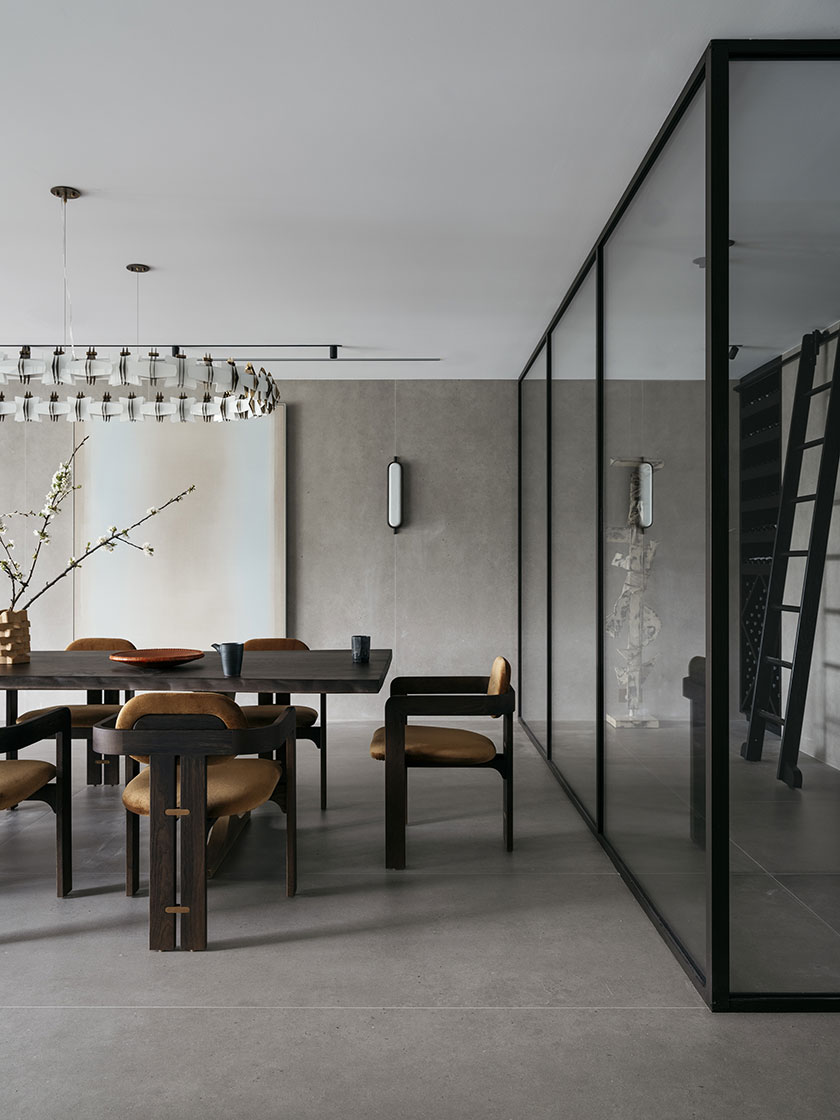 A dining area featuring a large dark wood table with custom chairs, a modern chandelier, and glass partitions, designed by Nina Maya Interiors.