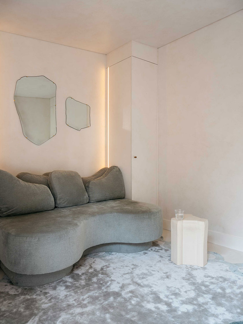 Stylish seating area with a curved grey sofa, abstract mirrors, and soft lighting, designed by Nina Maya Interiors