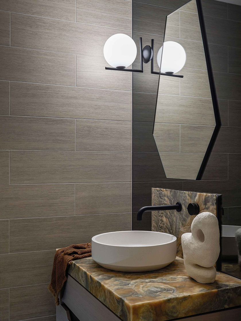 A contemporary bathroom in the Jewel Apartment by Nina Maya Interiors, featuring a round vessel sink, marble countertop, geometric mirror, and modern wall sconce.