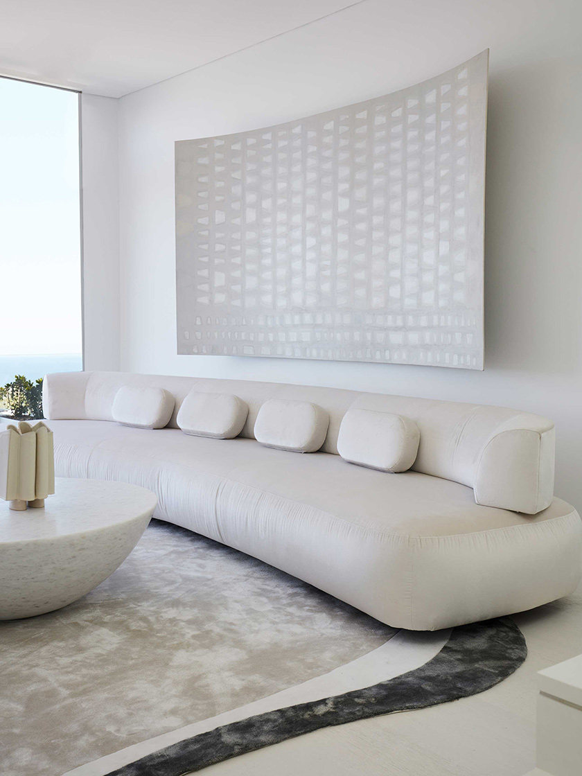 Minimalist living room with a curved white sofa, abstract wall art, and a round marble coffee table, designed by Nina Maya Interiors