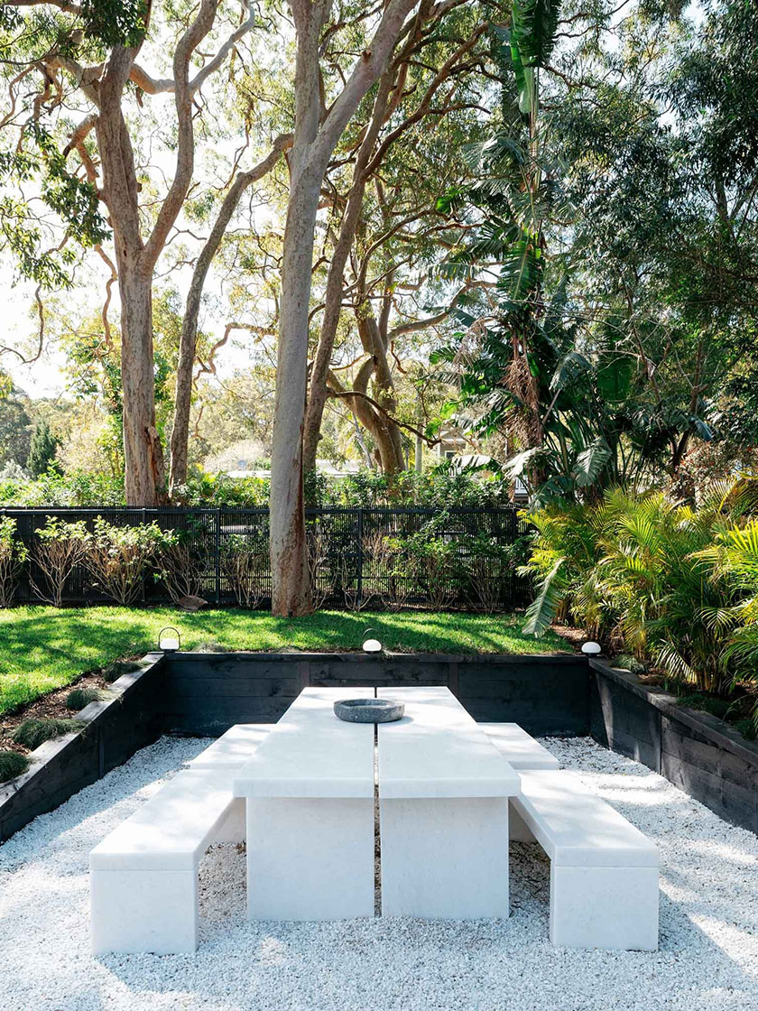 Chic outdoor dining area with a white stone table and benches surrounded by lush greenery, designed by Nina Maya Interiors.