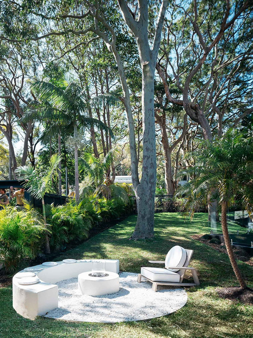 Serene garden seating area with a circular white stone bench and chair, nestled among tall trees and lush greenery, designed by Nina Maya Interiors.