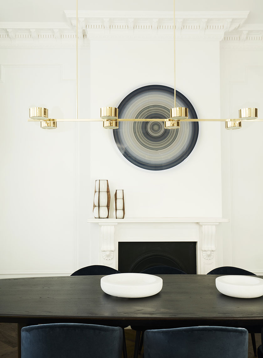 A bright living room featuring a curved gray sofa, a glass coffee table, and green marble side tables, with a backlit art piece on the wall. Interior design by Nina Maya Interiors.