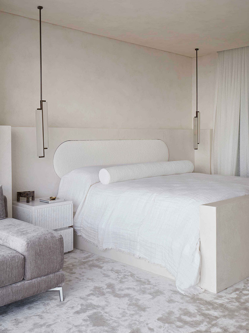 Bright bedroom with white bedding, a grey lounge chair, and an ocean view.