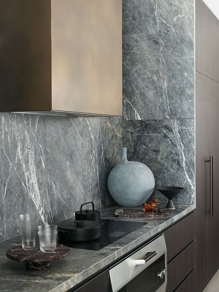 Close-up of the kitchen area designed by Nina Maya Interiors, focusing on the dark cabinetry, marble countertop, and framed geometric artwork on the wall. Decorative elements include a vase with green flowers and a sculptural table lamp.