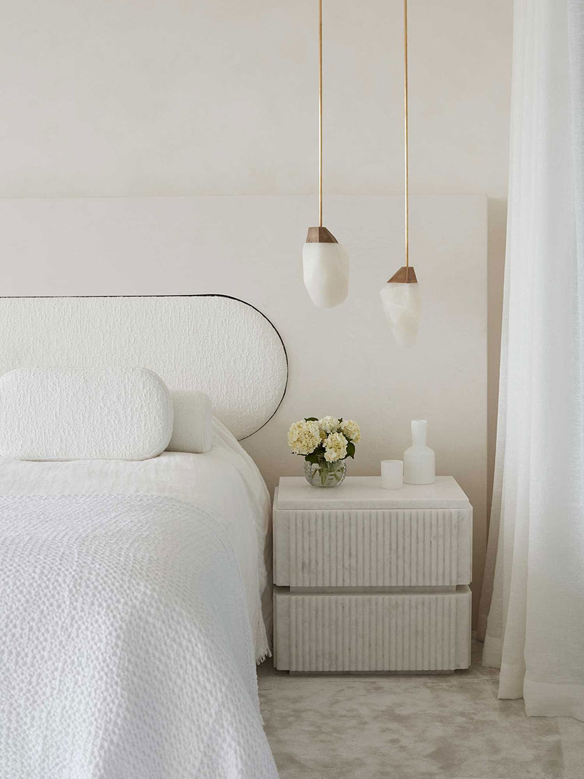 Elegant bedroom with white bedding, hanging pendant lights, and a marble bedside table, designed by Nina Maya Interiors.