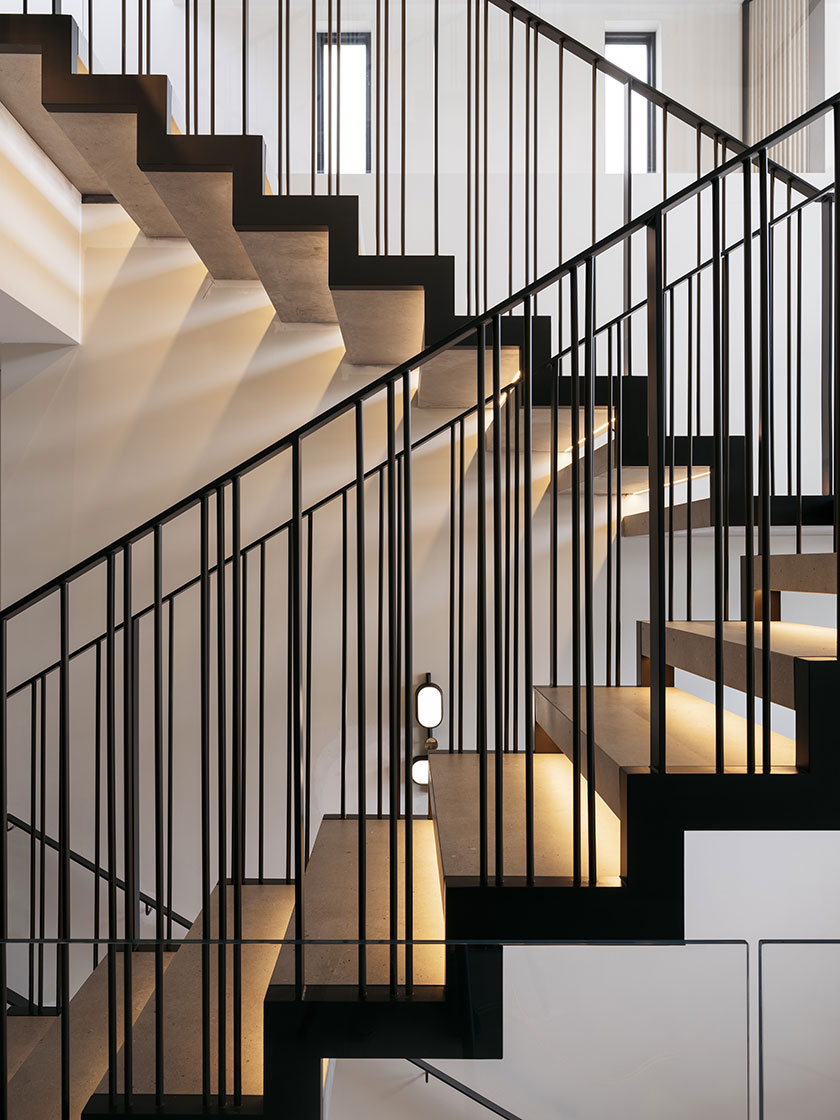 A close-up of the modern floating staircase designed by Nina Maya Interiors, featuring bronze and porcelain steps with sleek black railings, illuminated by subtle lighting.