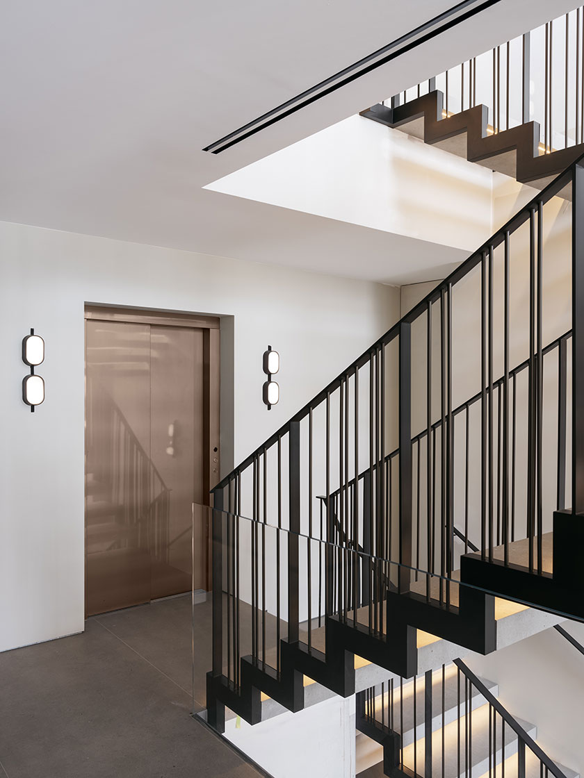 A view of the floating staircase and elevator area in Residence R, designed by Nina Maya Interiors, showcasing the staircase’s elegant black railings and the bronze elevator door.