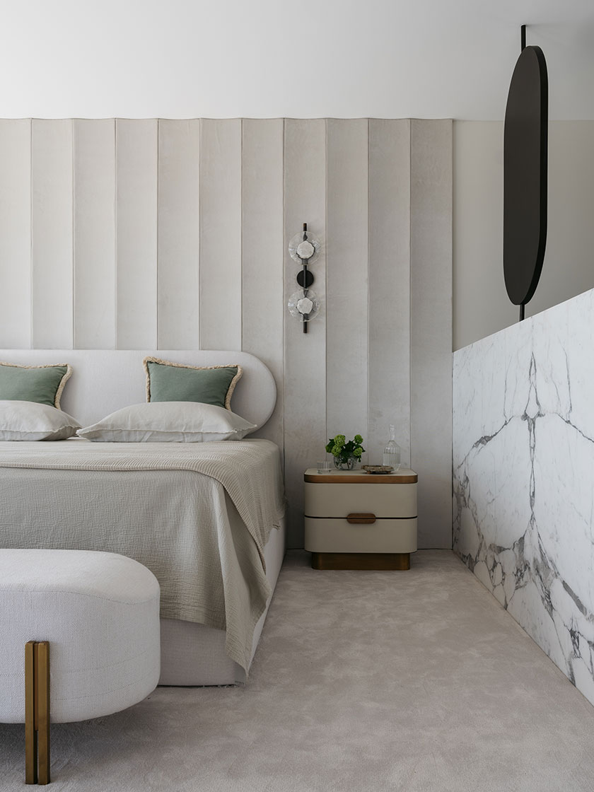 A contemporary bedroom featuring a neutral color palette, a plush bed with green pillows, and a marble partition wall. Interior design by Nina Maya Interiors.