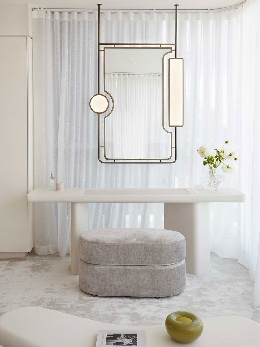 Stylish vanity area with a hanging mirror, grey stool, and minimalist decor, designed by Nina Maya Interiors.