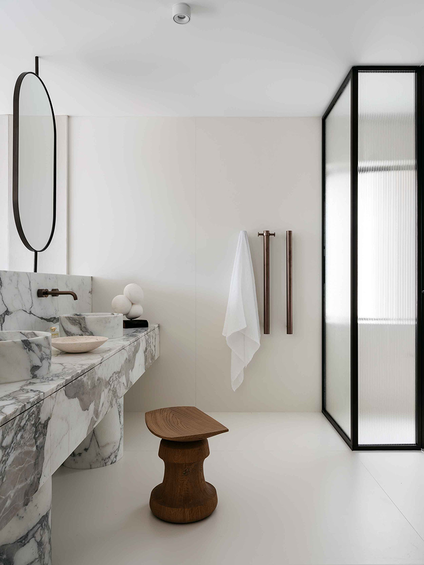 A luxurious bathroom with a marble vanity, a wooden stool, and modern fixtures. Interior design by Nina Maya Interiors.