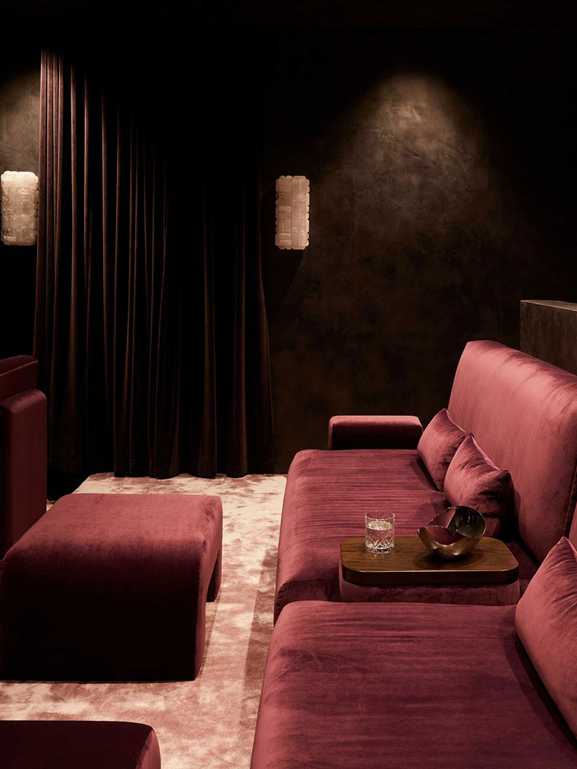 Luxurious home theater with deep red velvet seating and dark walls, designed by Nina Maya Interiors.