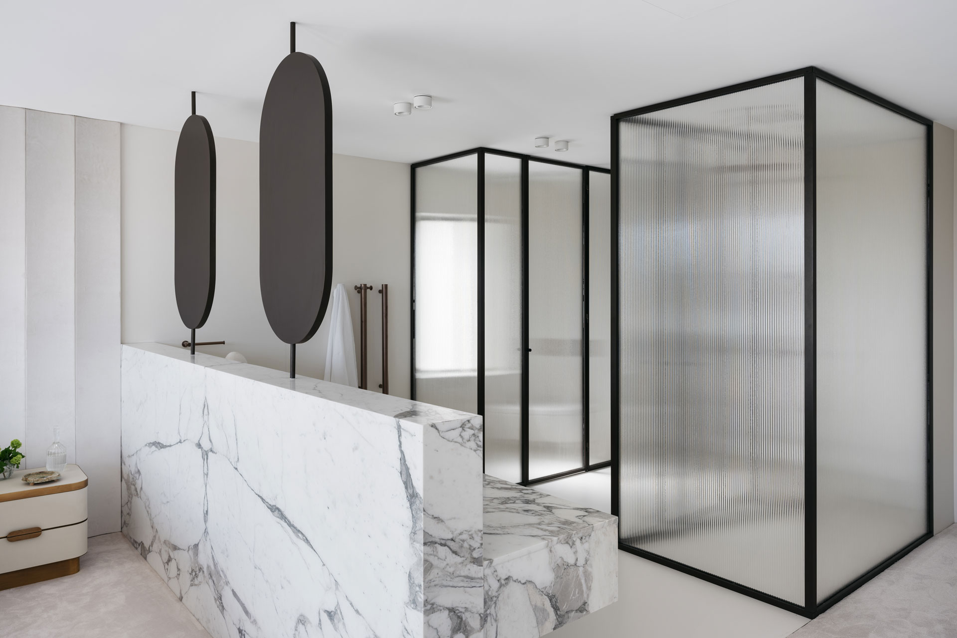 A view of the bathroom with marble finishes, modern fixtures, and frosted glass partitions. Interior design by Nina Maya Interiors.