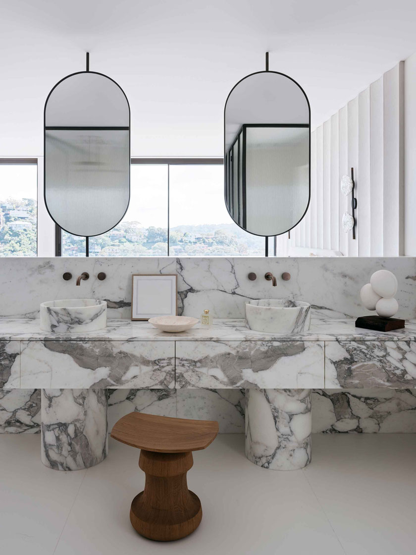 The bathroom's marble vanity with dual sinks, wooden stool, and minimalist decor. Interior design by Nina Maya Interiors.