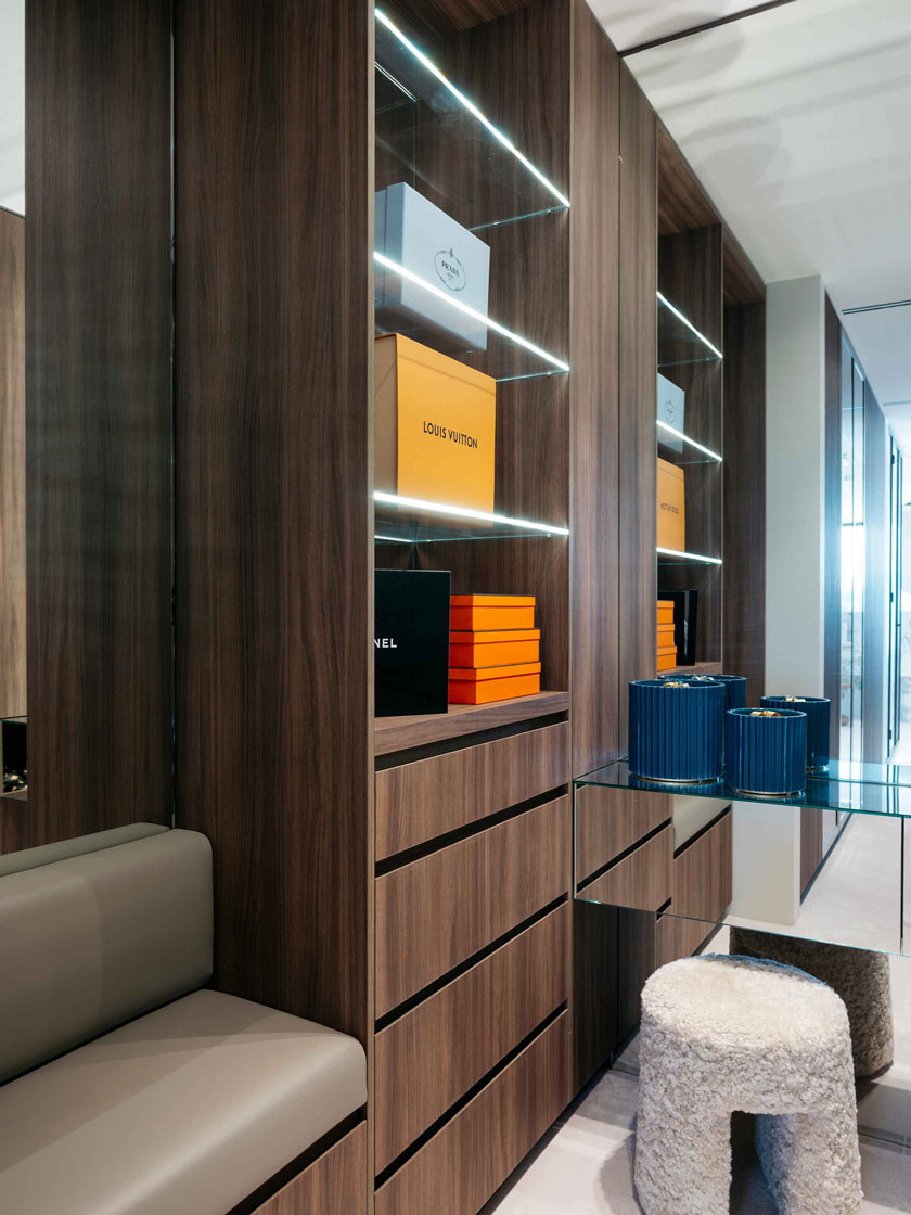 A modern dressing room with wooden cabinetry, LED lighting, and luxury brand boxes on display. Interior design by Nina Maya Interiors.