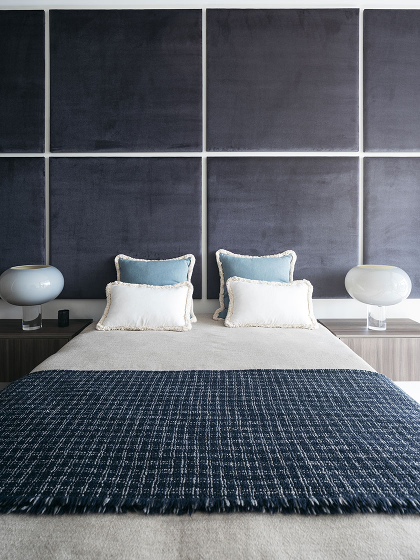 Modern bedroom by Nina Maya Interiors, featuring a bed with blue and white pillows, large bedside lamps, and a textured navy blue blanket.