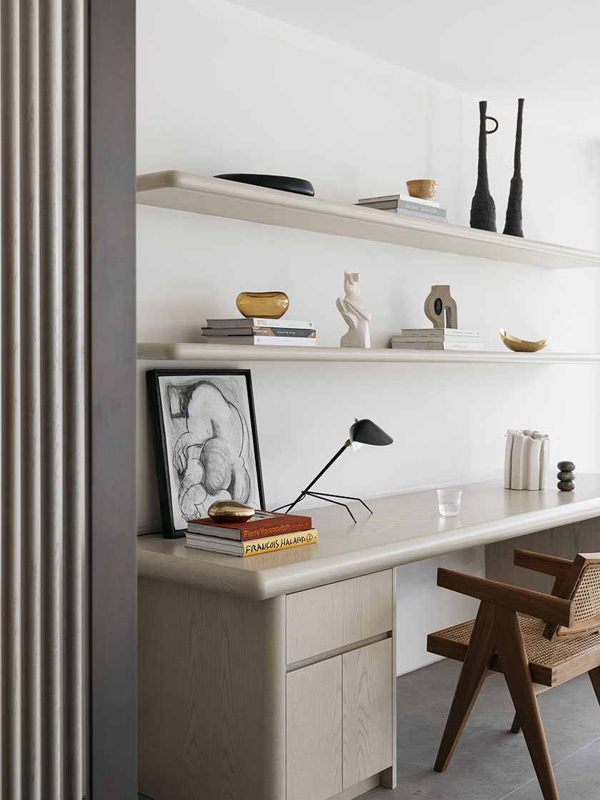 Stylish home office by Nina Maya Interiors, with a minimalist wooden desk, floating shelves adorned with decorative items, and a comfortable wooden chair.