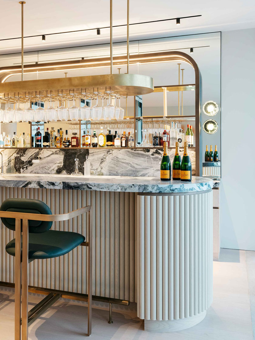 Luxurious bar area by Nina Maya Interiors, featuring a marble countertop, stylish gold bar stools, and an array of neatly arranged glassware.