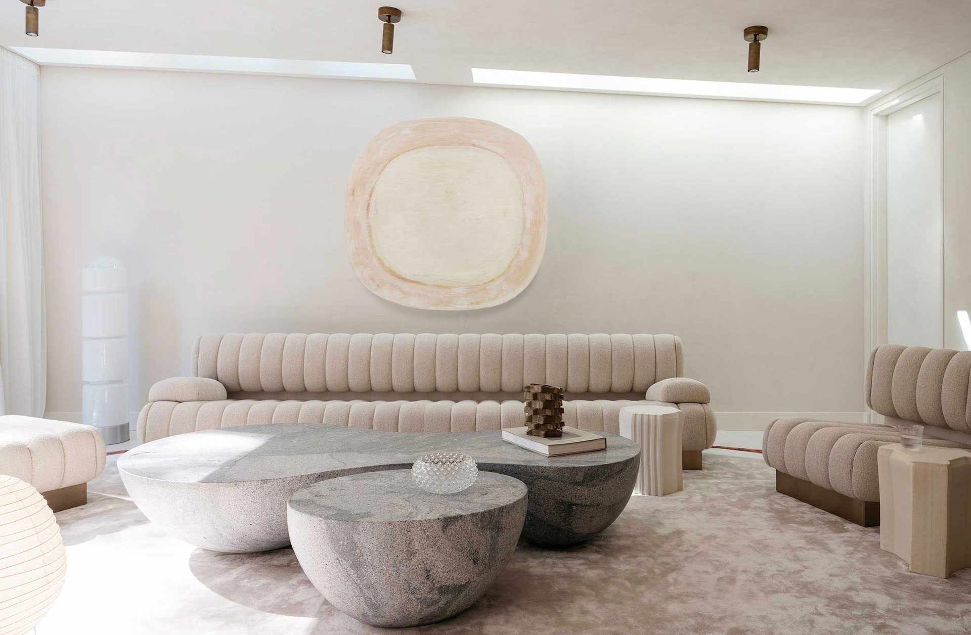 Contemporary living room with cream sofas, stone coffee tables, and a large wall art piece.