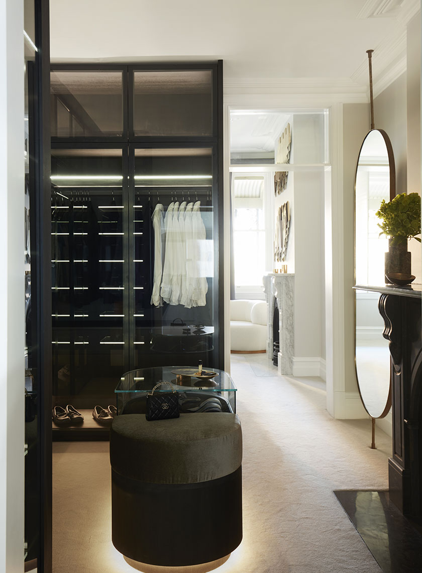 Stylish Walk-in Closet with Modern Accents: A chic walk-in closet showcasing a modern display of clothes and accessories behind glass doors, with a large mirror reflecting the elegant room beyond. Interior design by Nina Maya Interiors at Residence K, Potts Point.