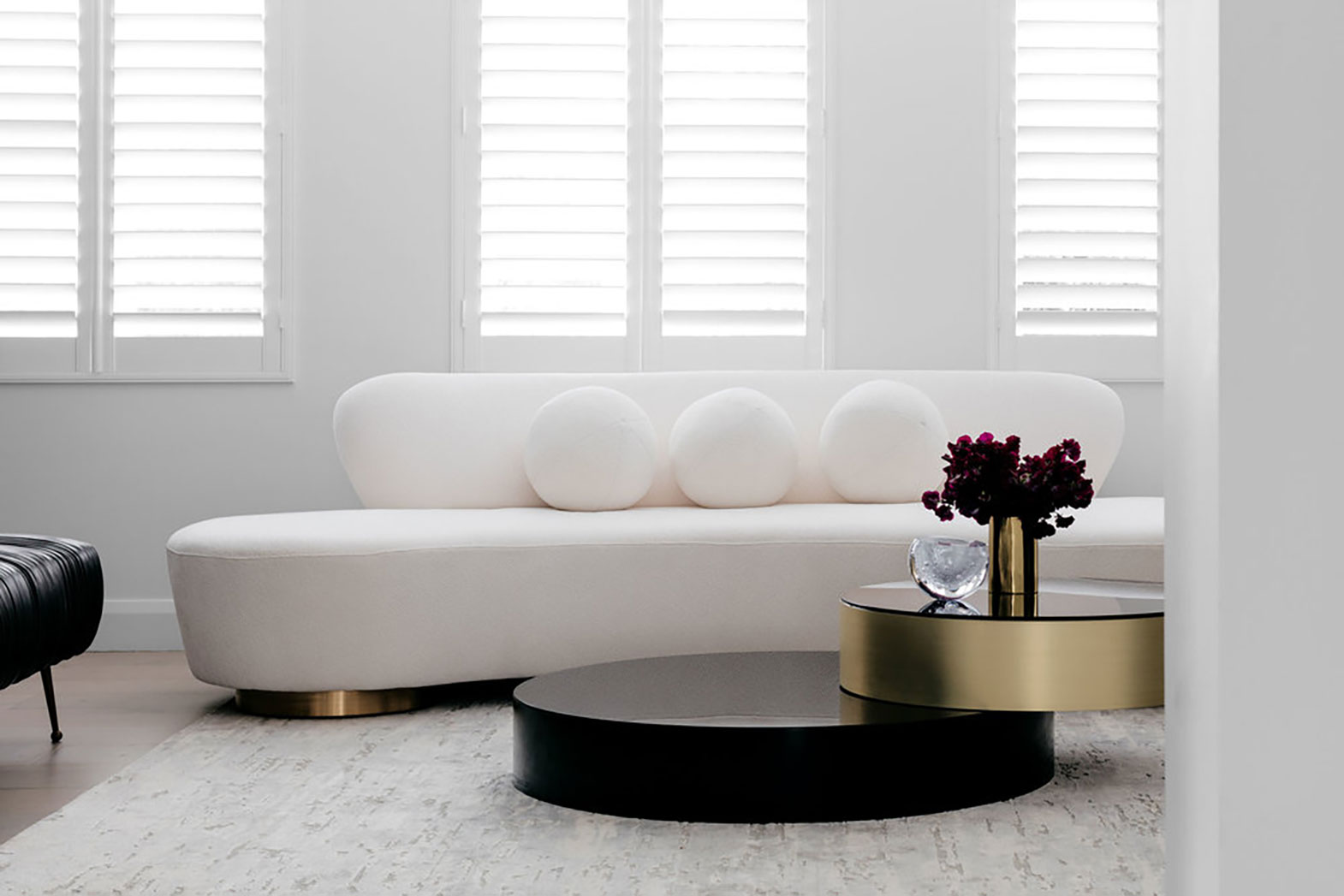 Minimalist living room with a white sofa, gold and black coffee table, and white shutters, designed by Nina Maya Interiors.