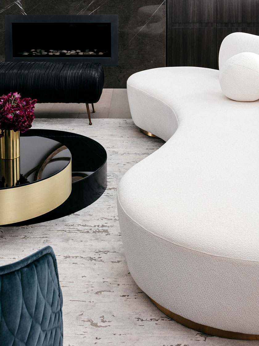 Close-up view of a gold and black coffee table with a glass ornament and flowers, white curved sofa in the background, designed by Nina Maya Interiors.