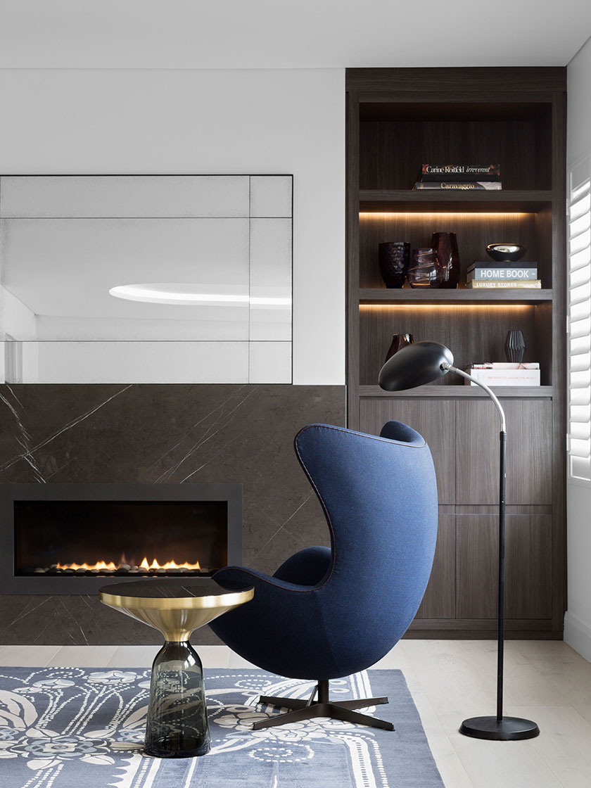 Cozy reading nook with a blue chair, modern fireplace, and built-in bookshelves, designed by Nina Maya Interiors.