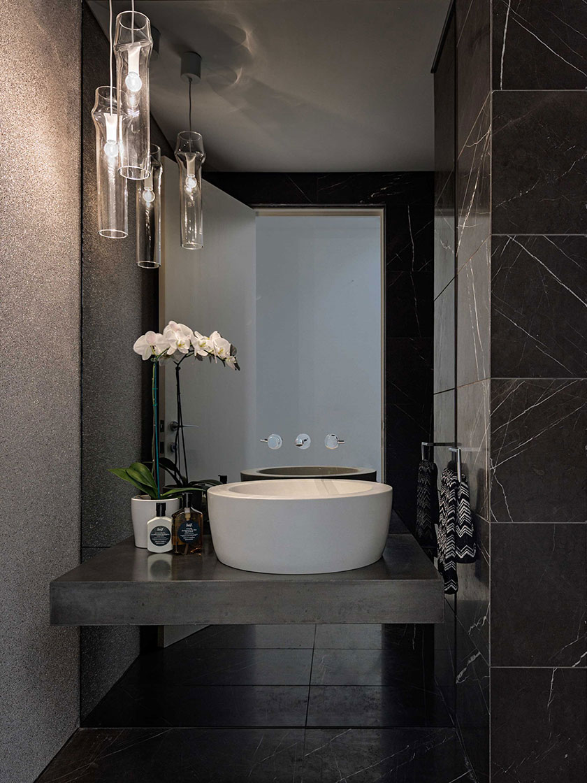 Elegant bathroom with a white vessel sink, black marble tiles, and pendant lighting, designed by Nina Maya Interiors.