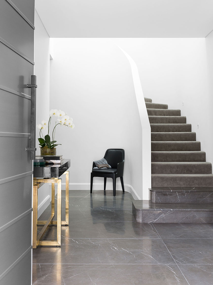 Modern entryway with a black chair, gold console table, and staircase, designed by Nina Maya Interiors.