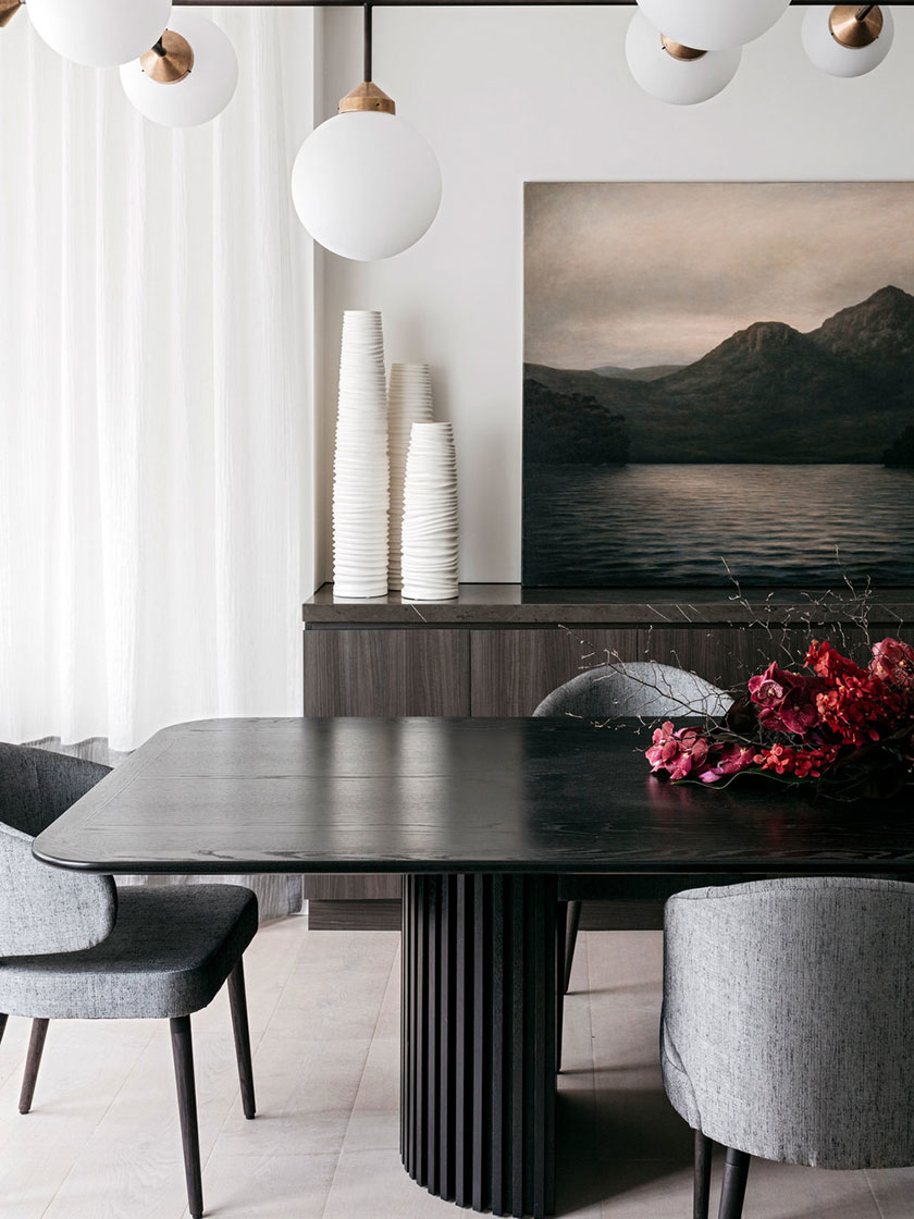 Modern dining area with a black table, grey upholstered chairs, and contemporary art on the wall, designed by Nina Maya Interiors