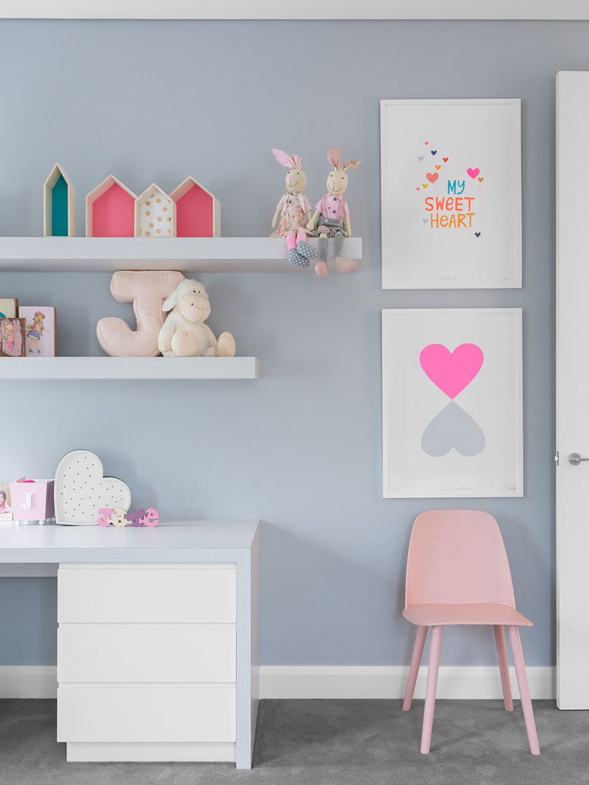 Child's room with a pink chair, white desk, floating shelves, and playful decor, designed by Nina Maya Interiors.